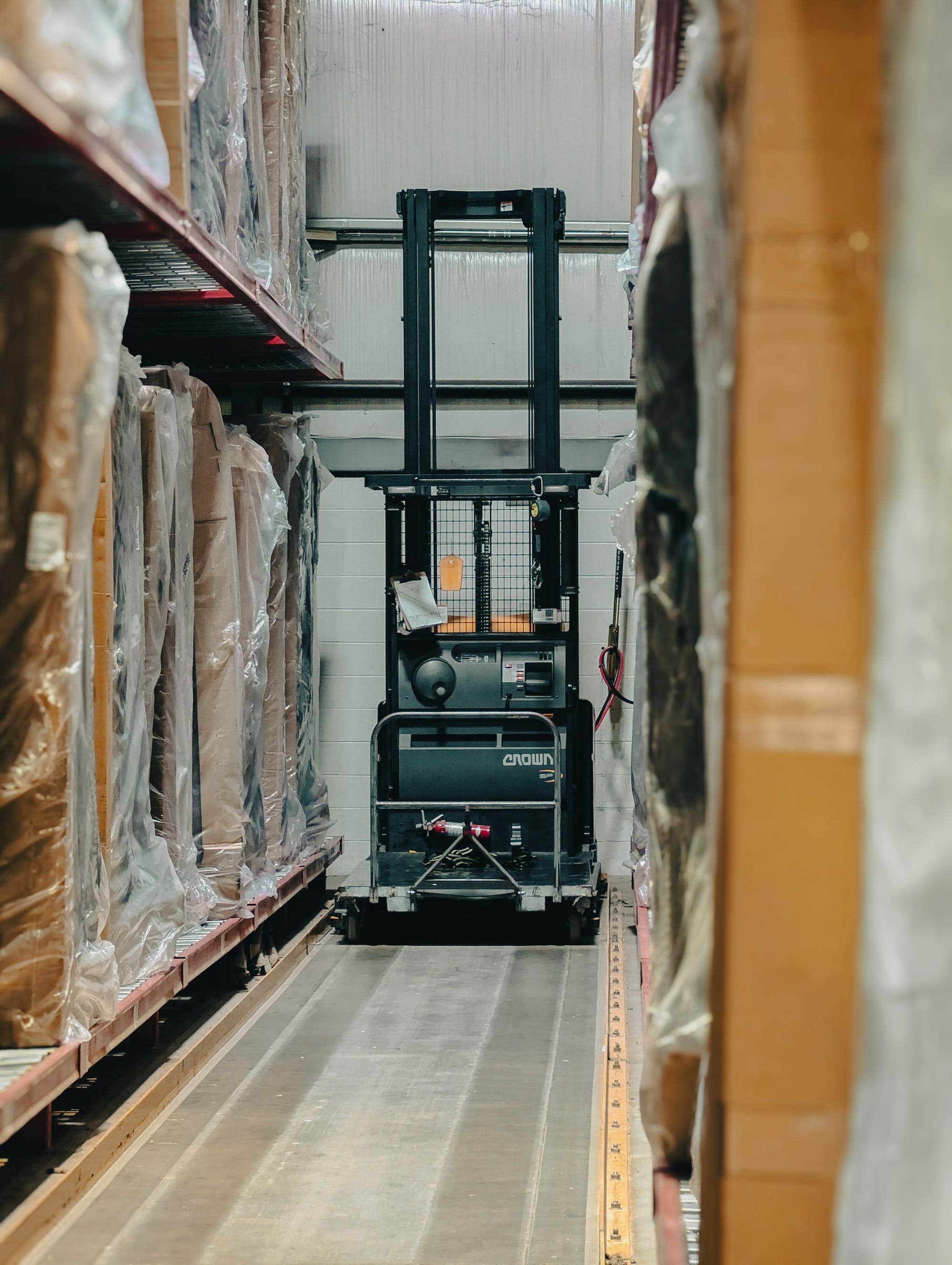 A forklift between tall shelves of packaged inventory in a warehouse.